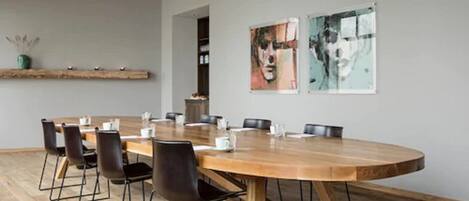 A conference room with a wooden table, black chairs, and two framed artworks on the wall.