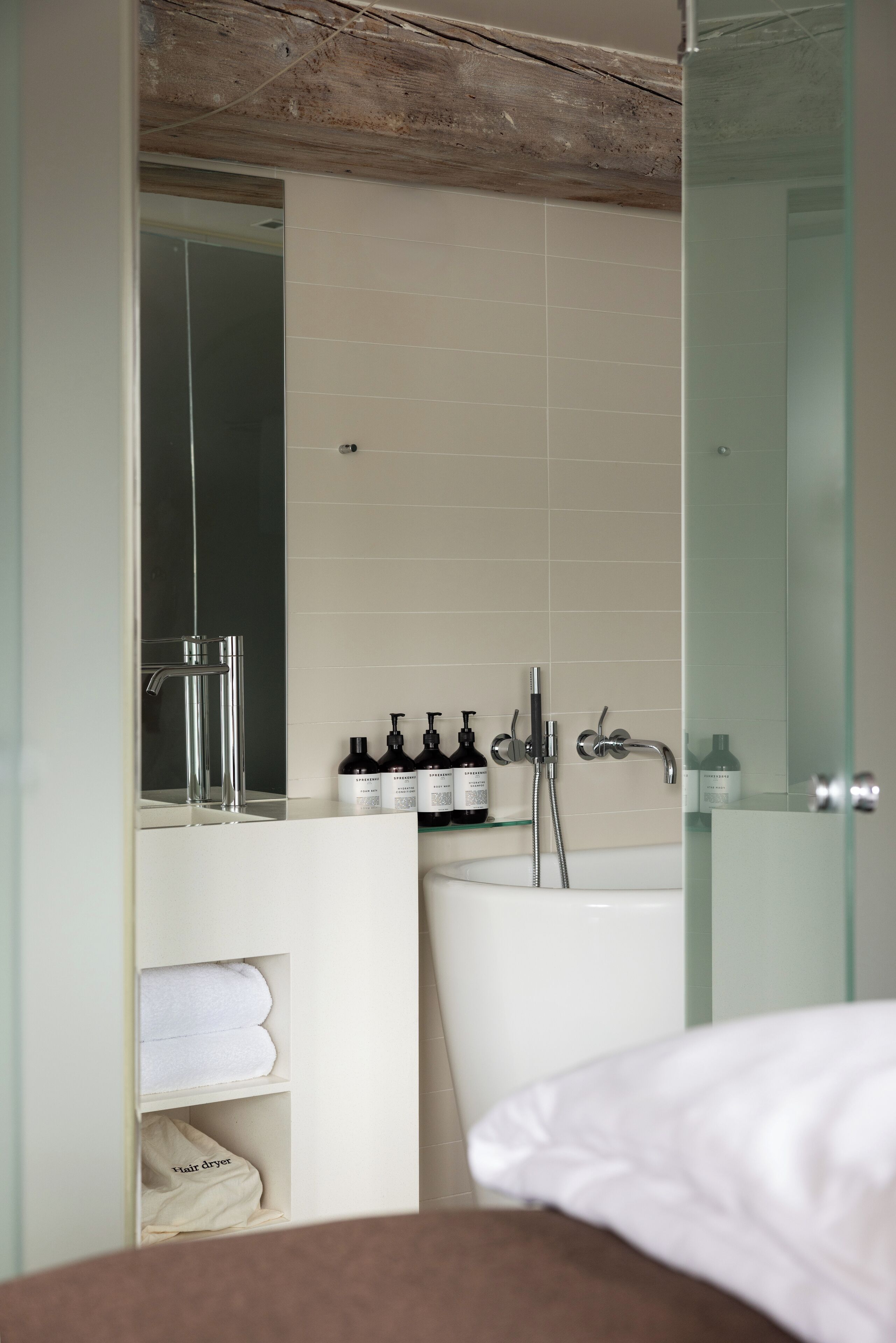 Une salle de bain moderne avec une douche à parois de verre, un lavabo blanc et un miroir au-dessus. On trouve des articles de toilette sur le comptoir du lavabo, ainsi qu’un porte-serviettes avec des serviettes.