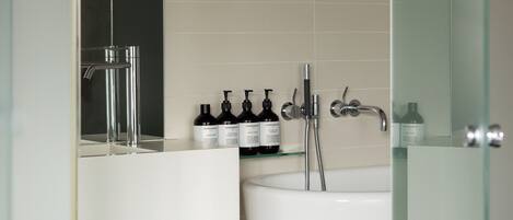 A modern bathroom with a glass shower enclosure, a white sink, and a mirror above it. There are toiletries on the sink counter and a towel rack with towels.