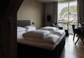 A hotel room with a large bed, a desk, and a view of a cityscape through a window.