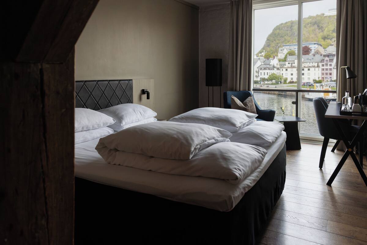 Ein Hotelzimmer mit einem großen Bett, einem Schreibtisch und Blick auf eine Stadtlandschaft durch ein Fenster.