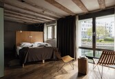 A modern bedroom with a wooden bed, a large window, and a view of a building across the water.
