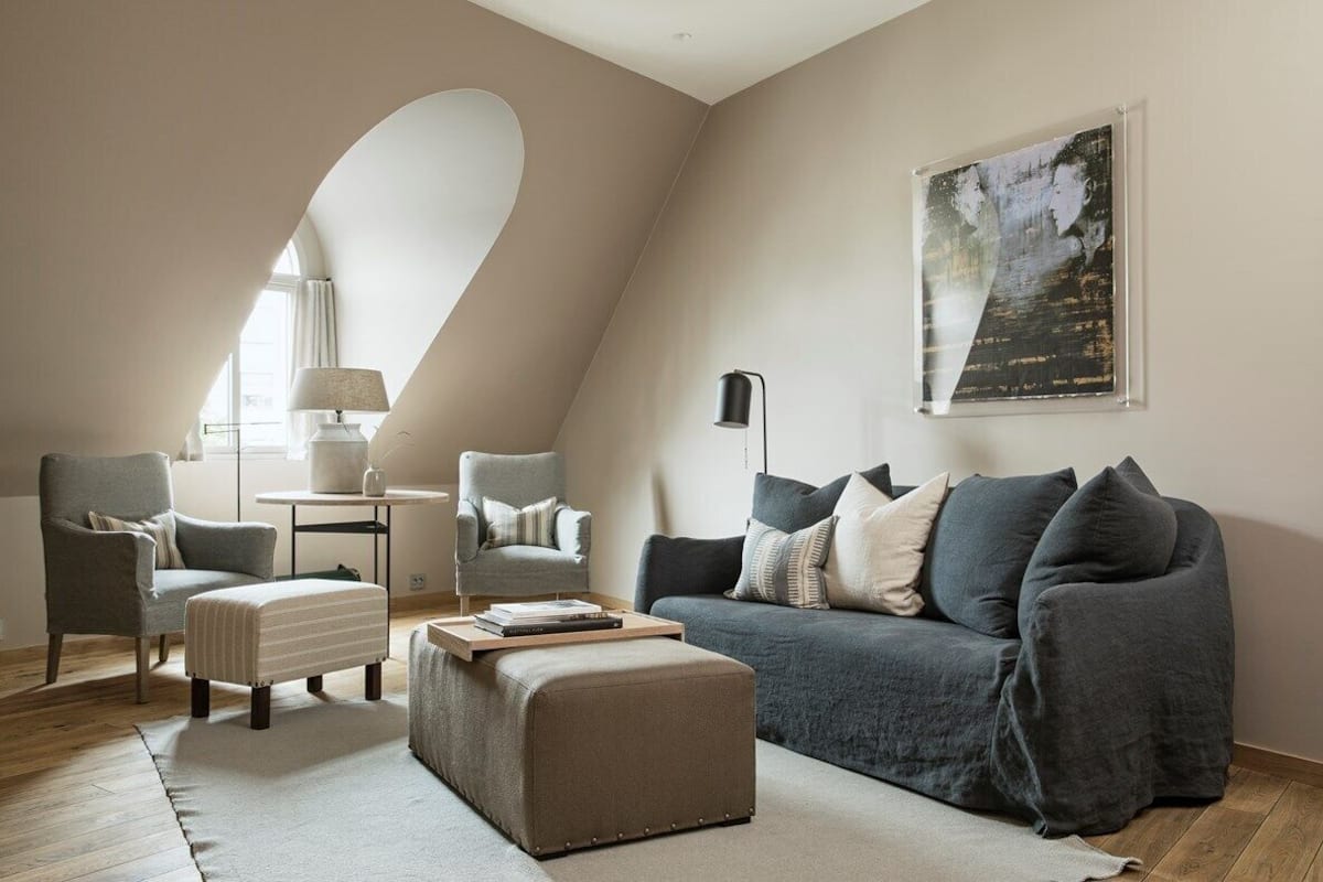 Ein modernes Wohnzimmer mit einem grauen Sofa, zwei Sesseln, einem kleinen Tisch und einer Lampe.
