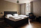A neatly made bed with white linens, a dark headboard, and a bedside table with a lamp.