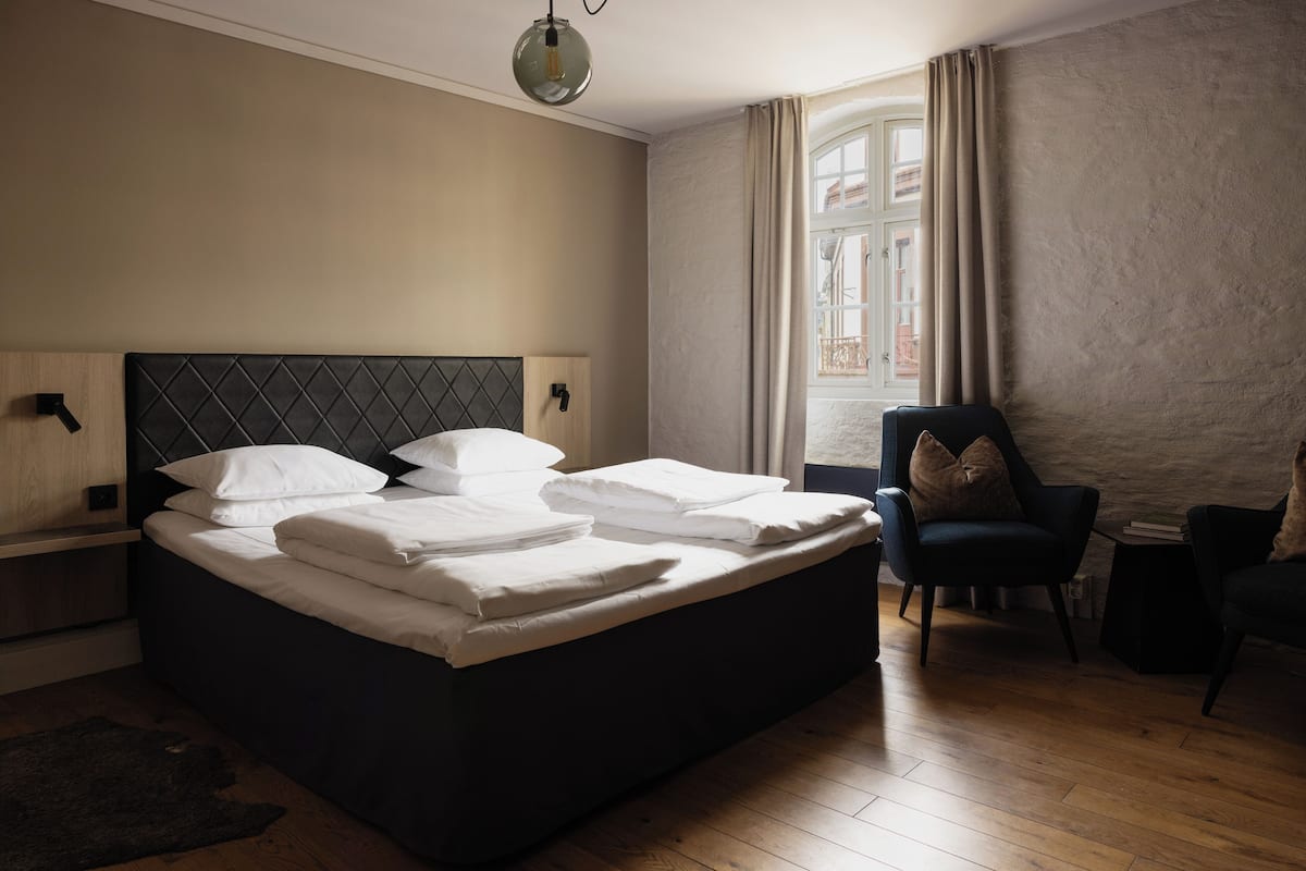 Ein ordentlich bezogenes Bett mit weißen Bettwäsche, einem dunklen Kopfteil und einem Nachttisch mit einer Lampe.