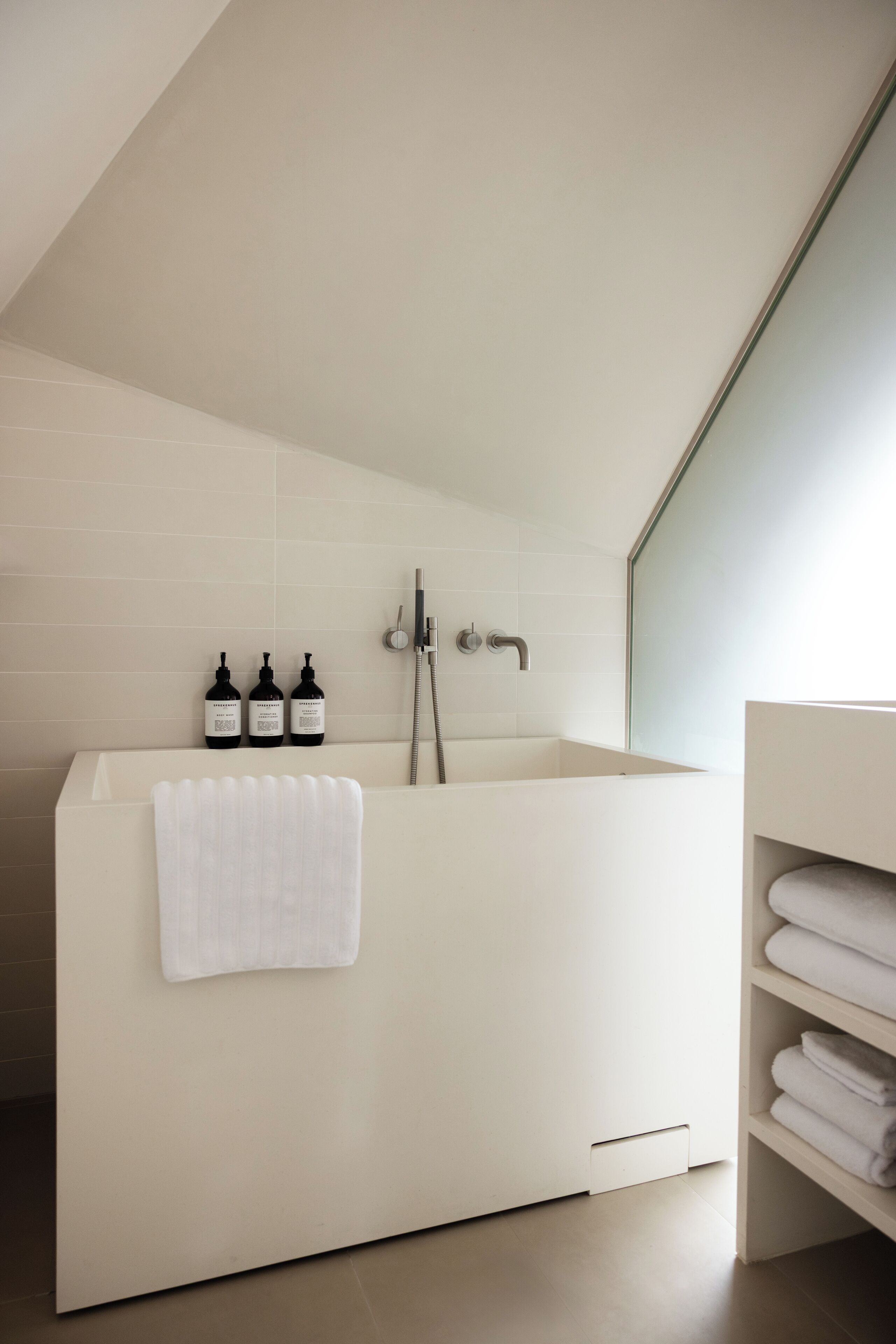 Un baño moderno con una bañera independiente, un cerramiento de ducha de vidrio y toallas ordenadas en un estante.