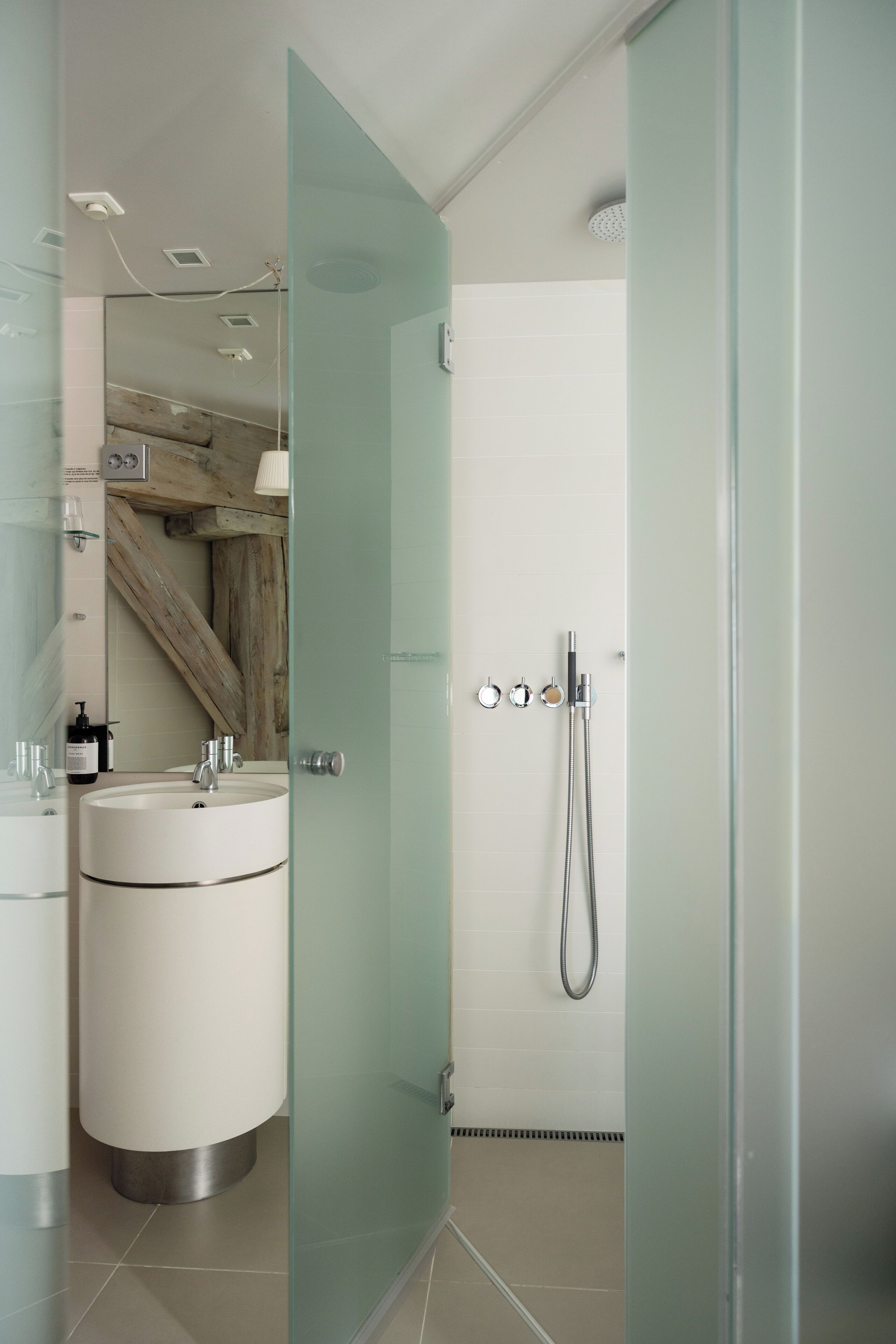 A modern bathroom with a glass shower enclosure, a white sink, and a wooden beam visible in the background.