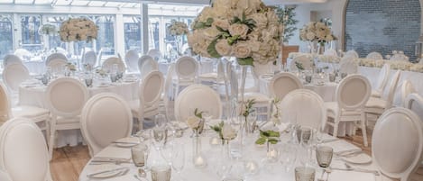 A banquet hall with round tables set for a formal event, featuring white chairs, elegant table settings, and large floral centerpieces.