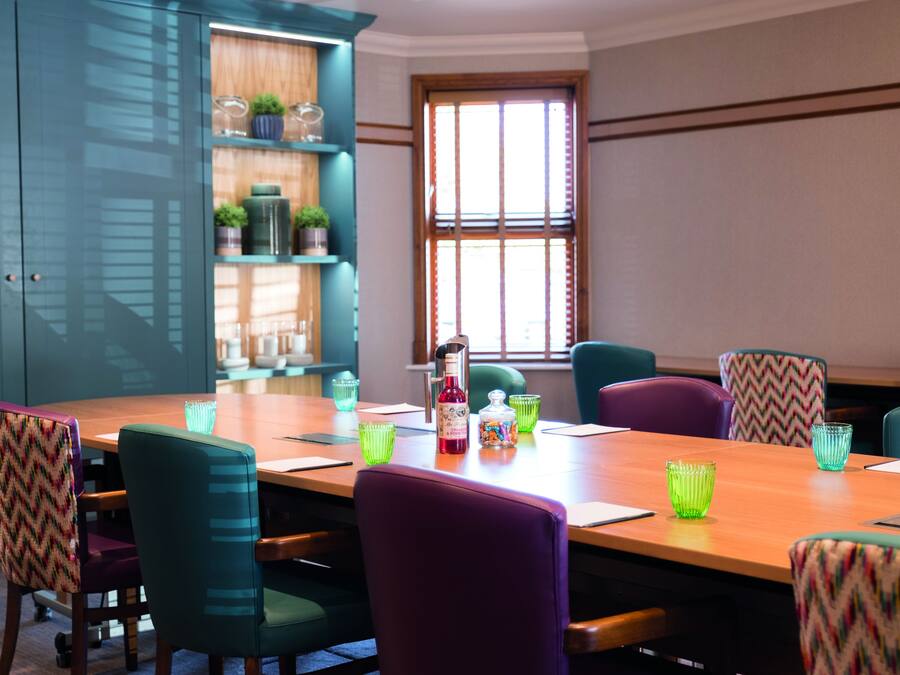 A conference room with a wooden table, teal chairs, and green glass cups.
