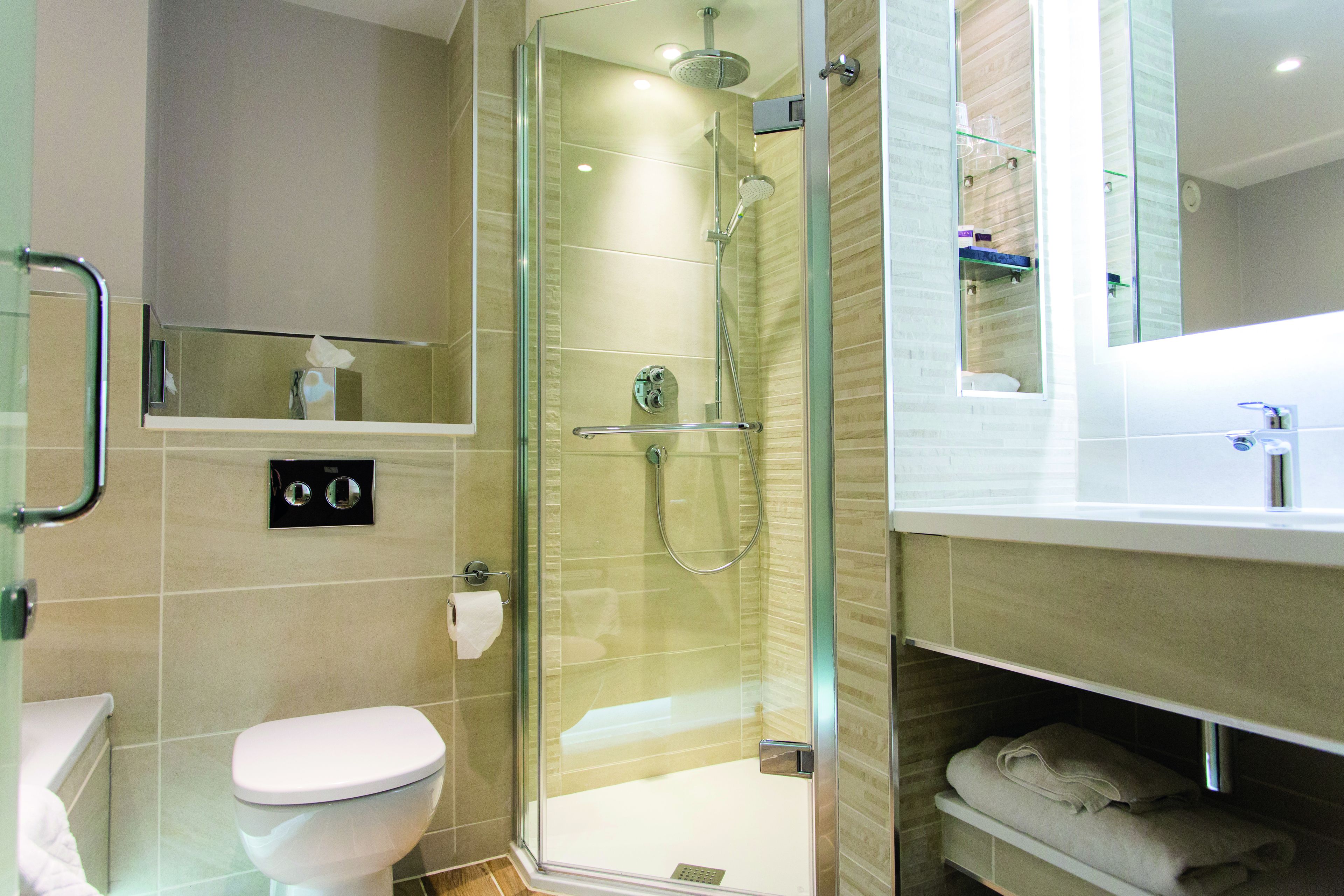 A modern bathroom with a glass-enclosed shower, a toilet, and a vanity with a mirror.