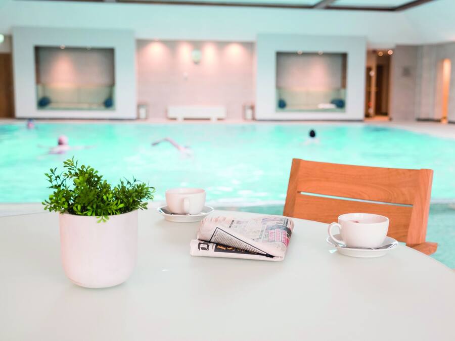 A pool area with a table, a chair, a potted plant, and a newspaper.