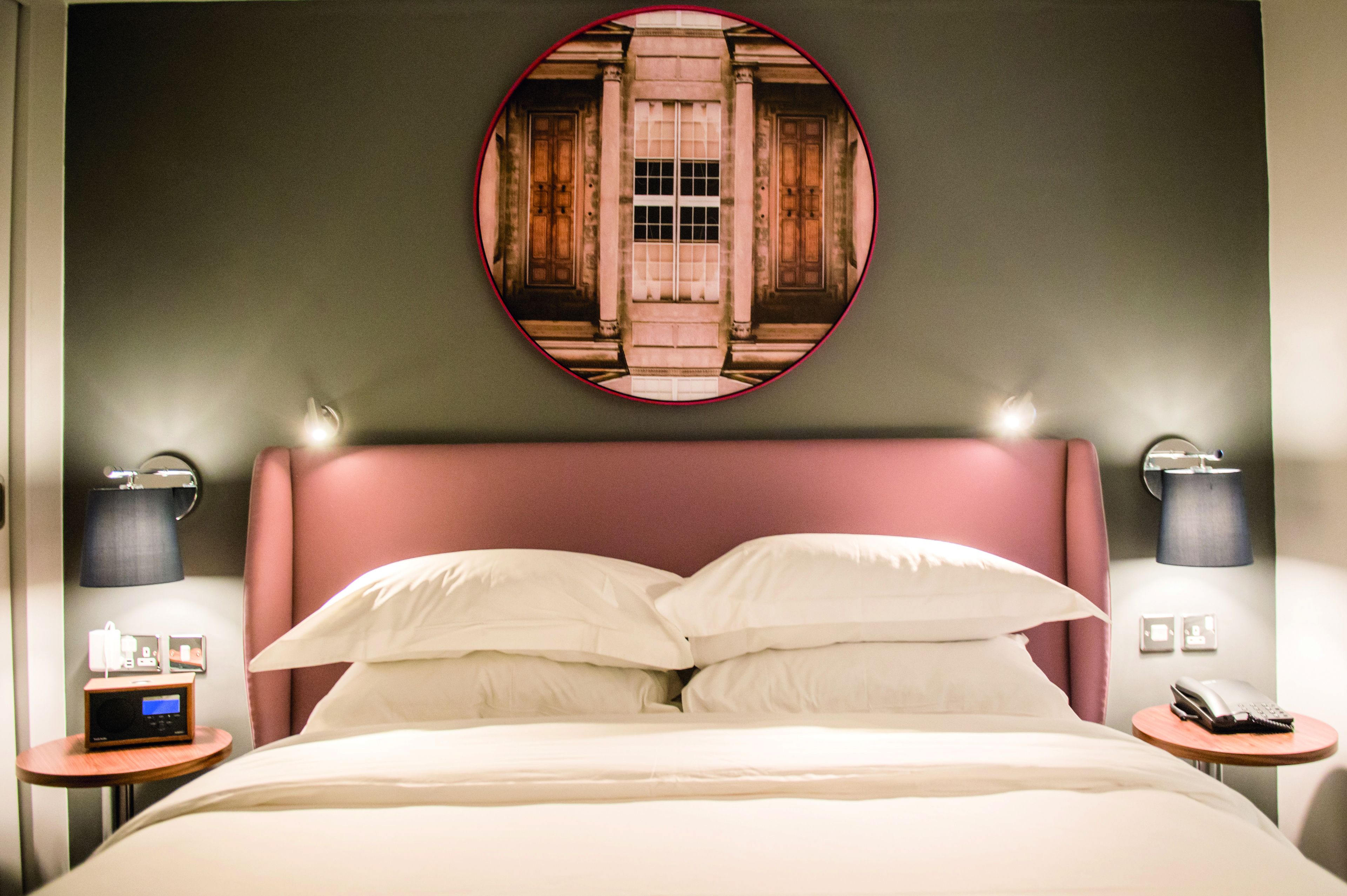 Une chambre d’hôtel avec un grand lit, deux tables de chevet, une lampe fixée au mur et un miroir rond.