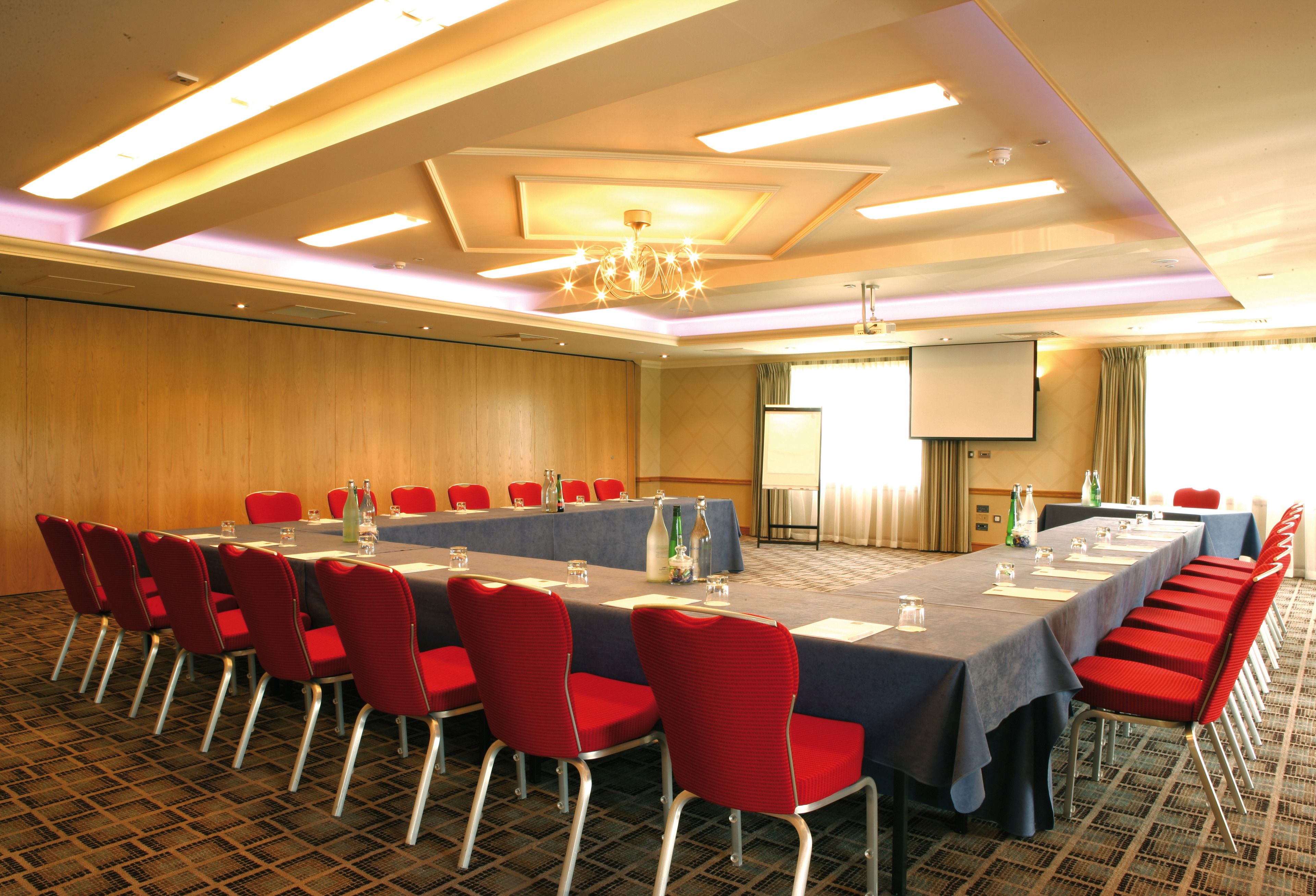 A conference room with a long table, red chairs, and a projector screen.