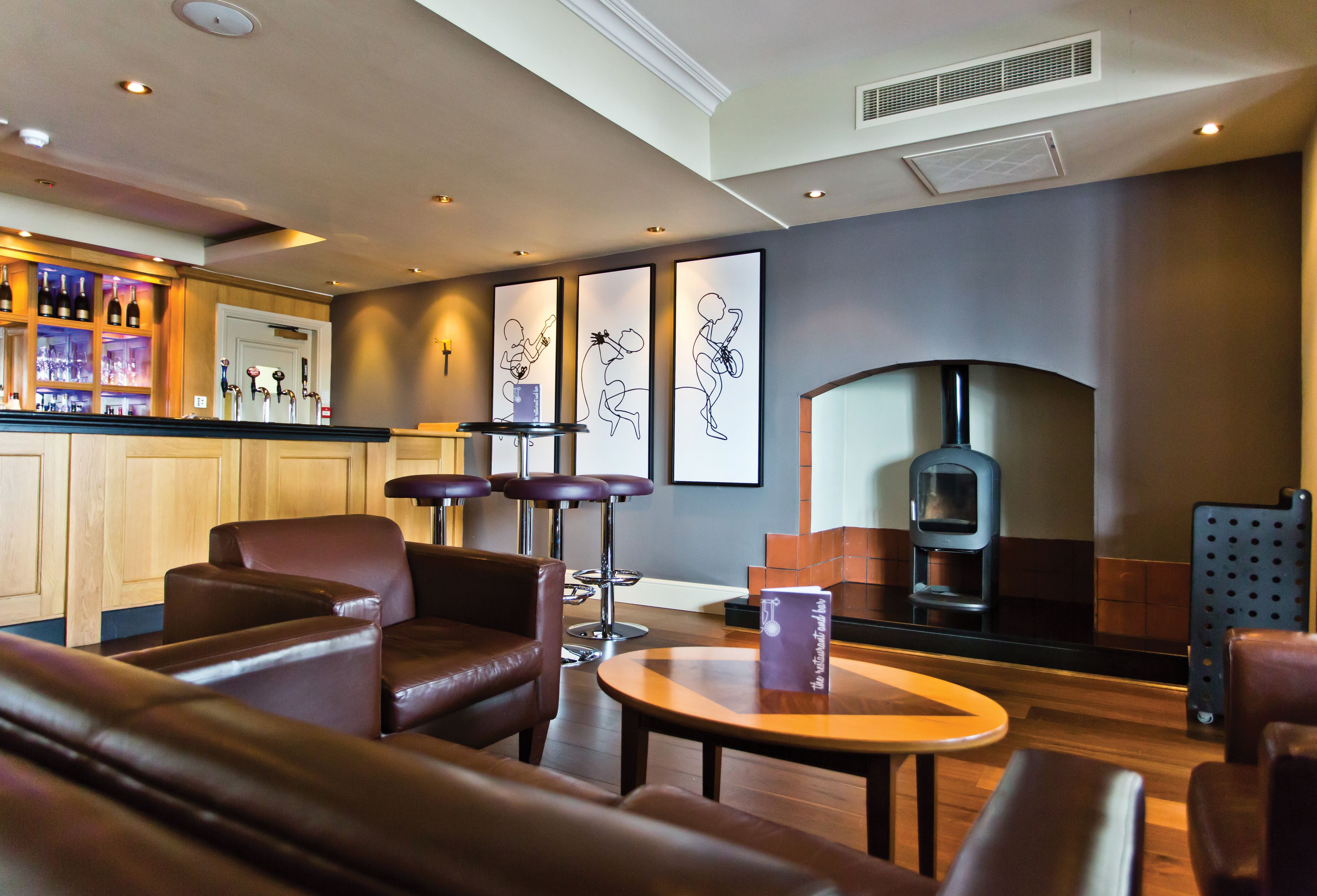 A modern lounge area with leather seating, a bar with wine bottles, and framed artwork on the wall.