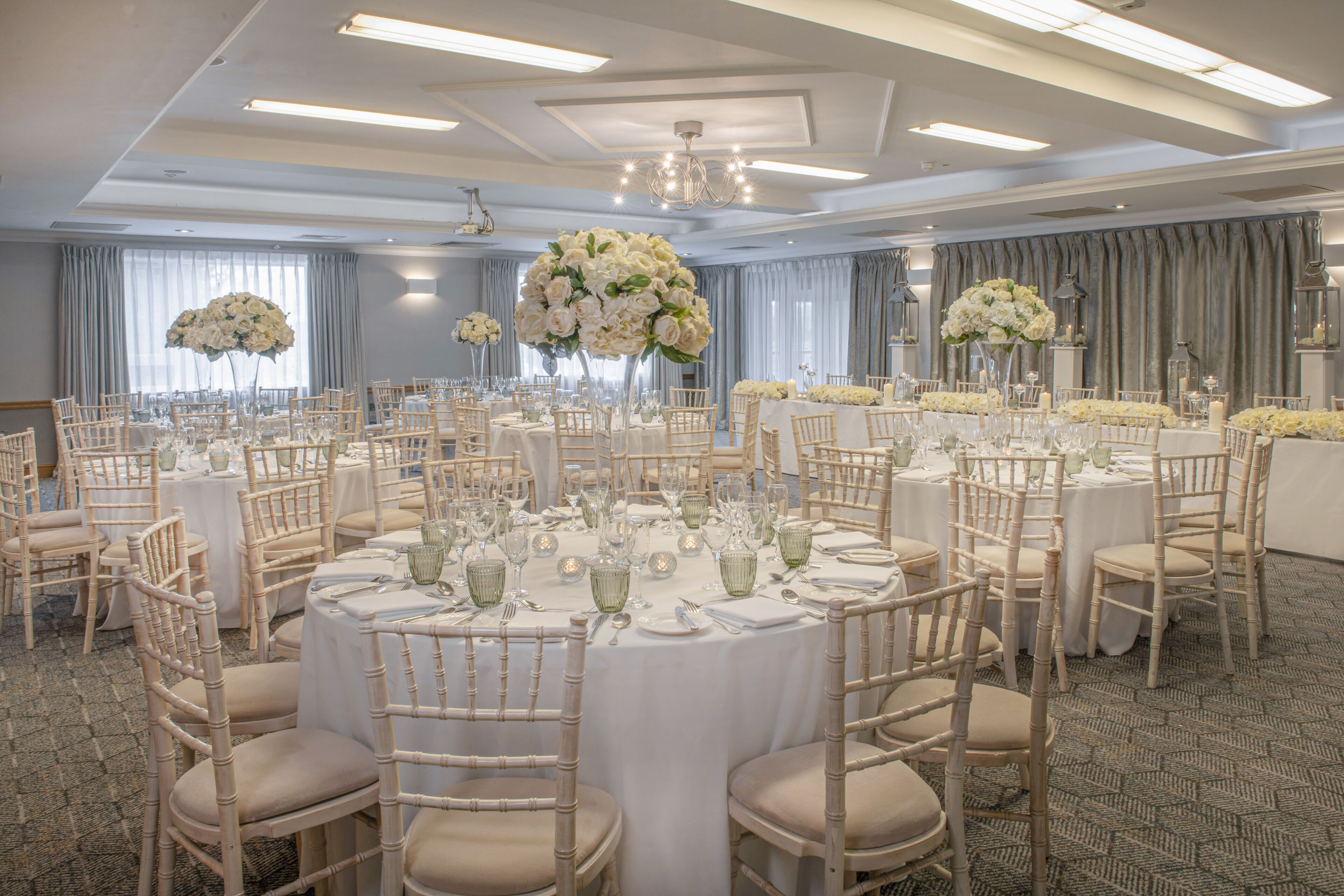 Ein Festsaal mit runden Tischen, weißen Tischdecken und floralen Mittelstücken.