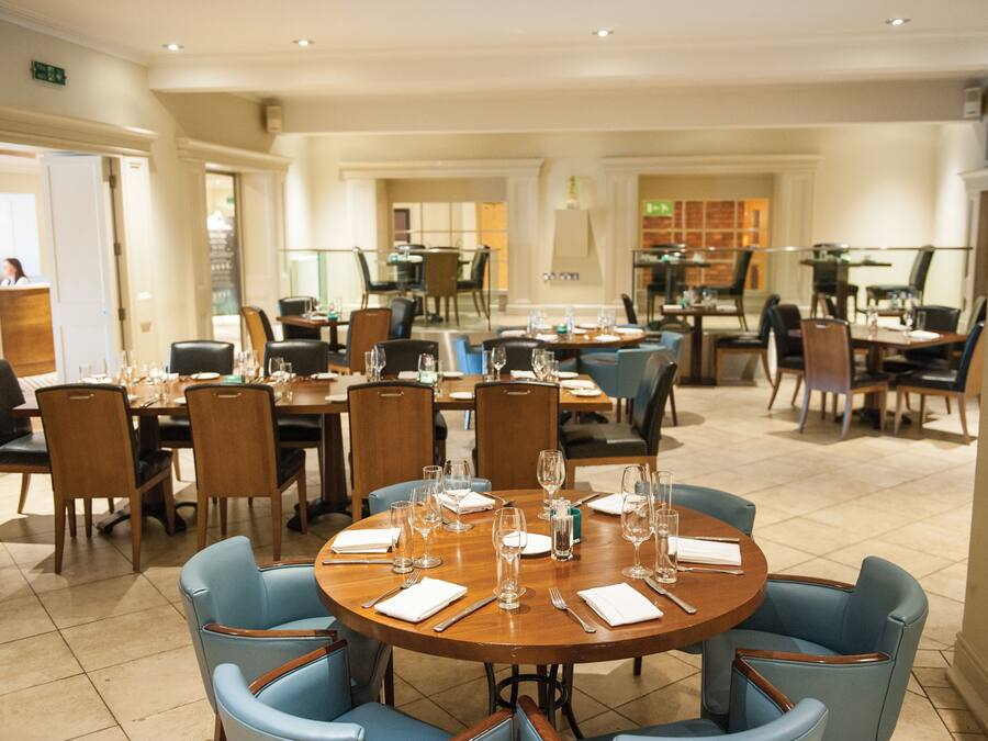 A spacious dining area with multiple round tables and blue chairs, equipped with wine glasses and cutlery.