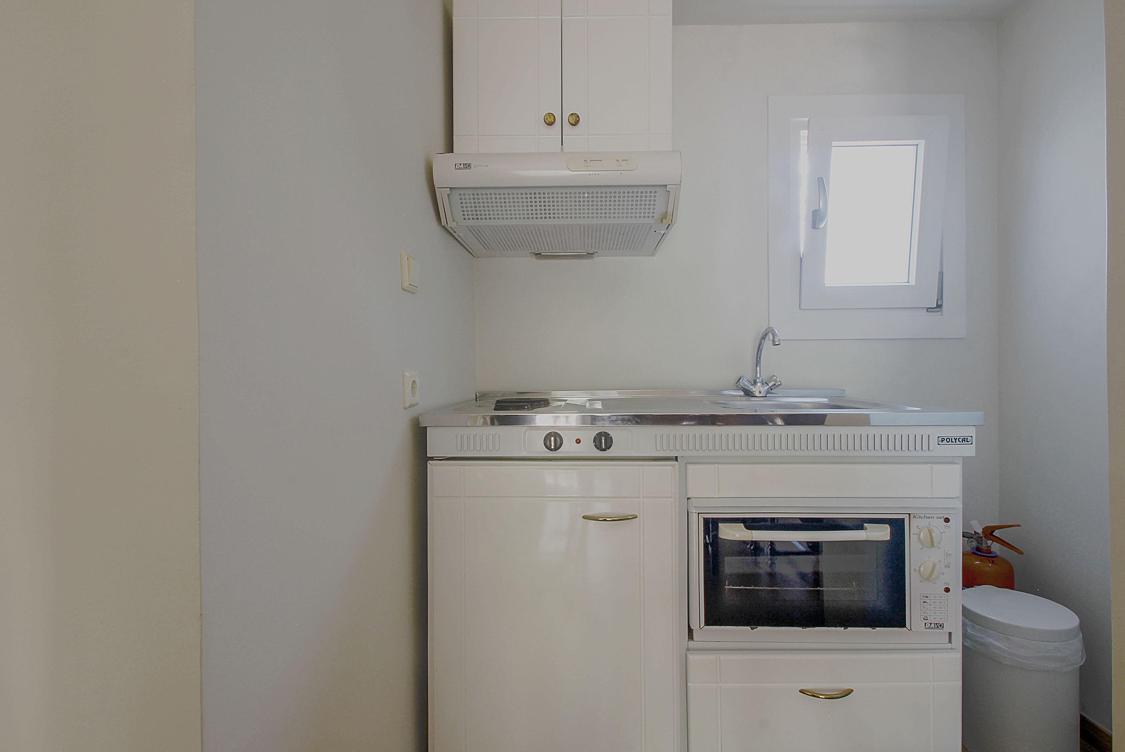 A compact kitchenette with a stove, oven, and a small window.