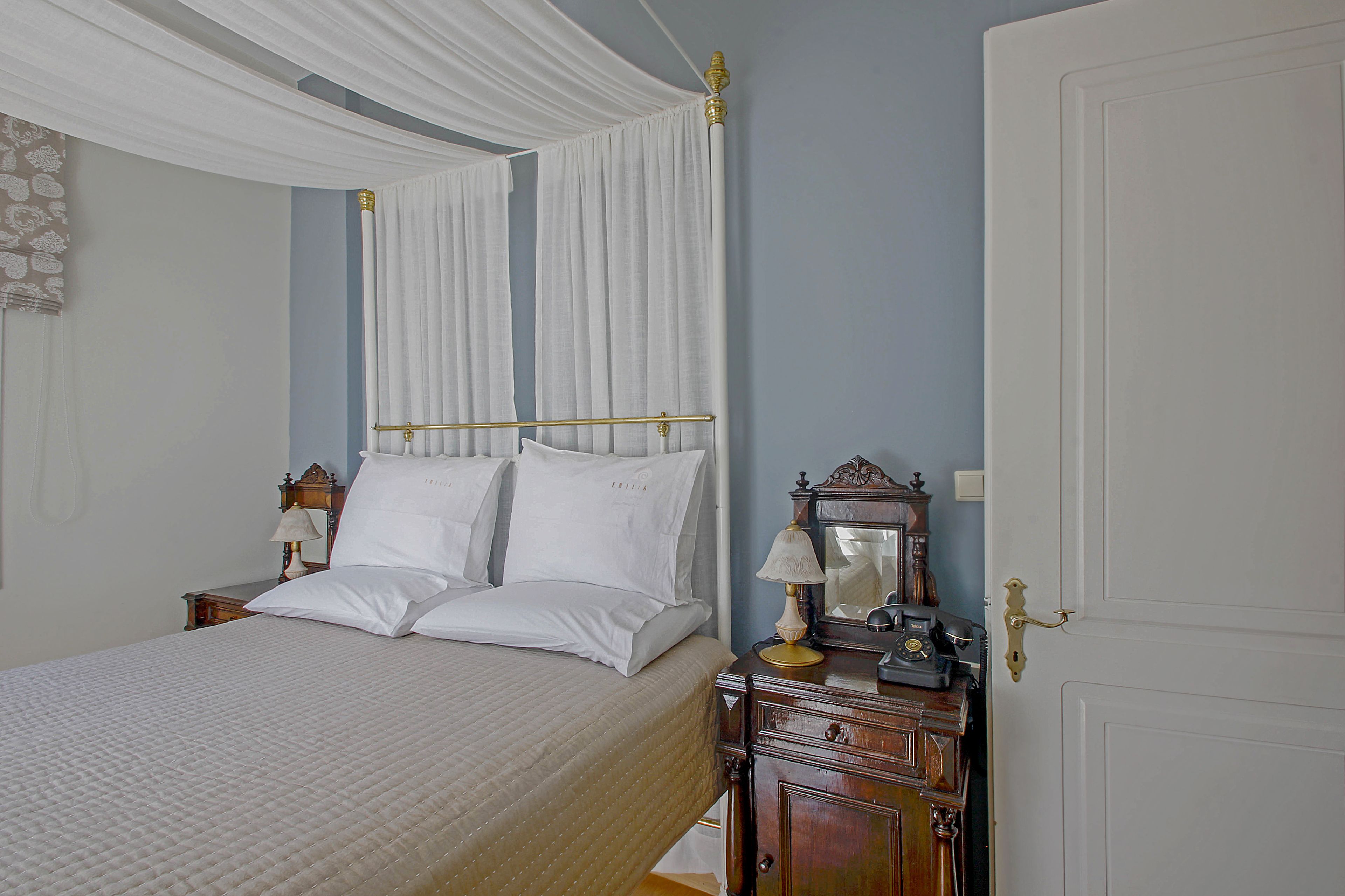 A neatly made bed with white linens, a wooden nightstand with a lamp, and a closed door.