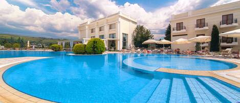 A large outdoor swimming pool surrounded by lounge chairs and umbrellas, with a building in the background.