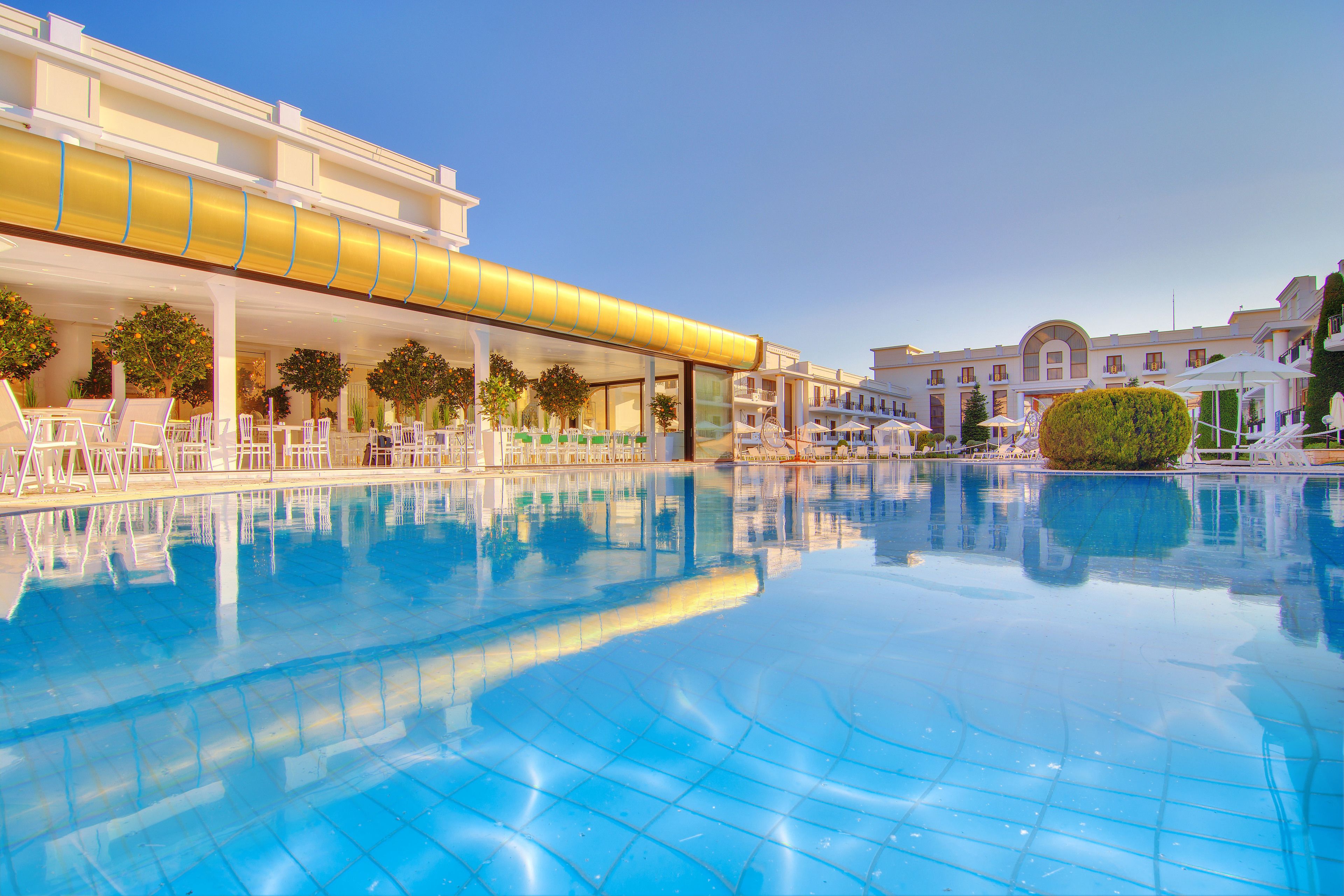 A swimming pool with clear blue water, surrounded by white lounge chairs and umbrellas.