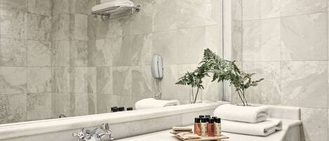 A modern bathroom with a large mirror, a sink, and a bathtub. There are towels and toiletries on the counter.