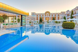 Zona de piscina de hotel con una piscina cristalina, tumbonas, sombrillas y un edificio con varios balcones.
