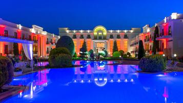 Un hotel con piscina central, varios balcones y una fachada bien iluminada.