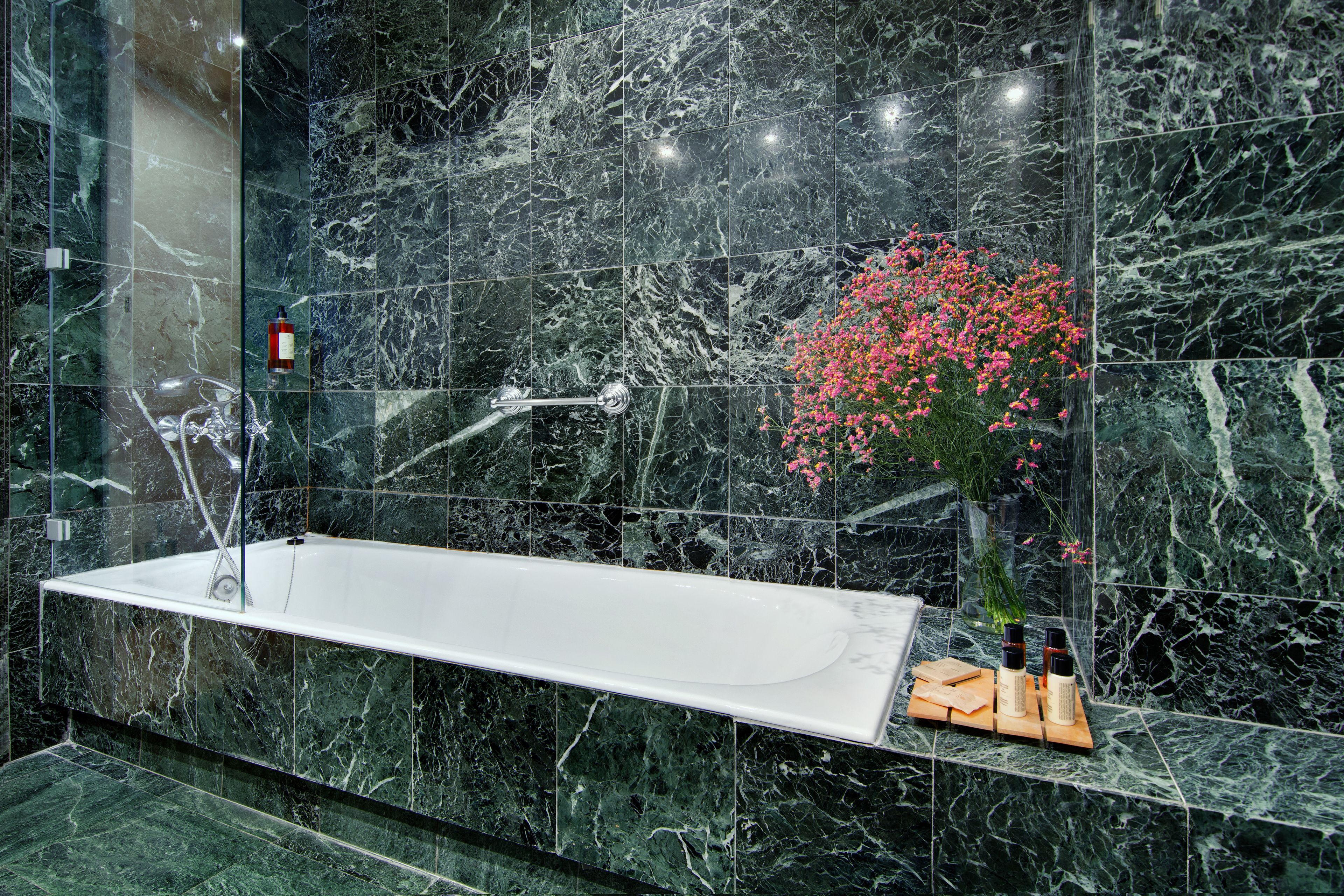 A modern bathroom with a large white bathtub, marble walls, and a small vase with pink flowers.
