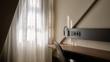 Una habitación de hotel moderna con escritorio, silla y regadera eléctrica con cables.