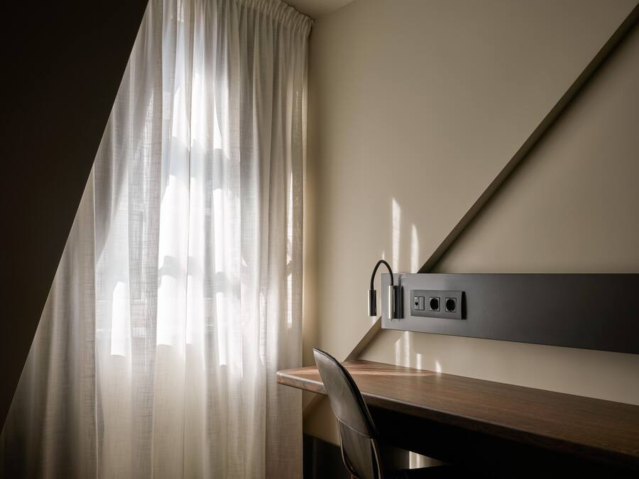 Una habitación de hotel moderna con escritorio, silla y regadera eléctrica con cables.