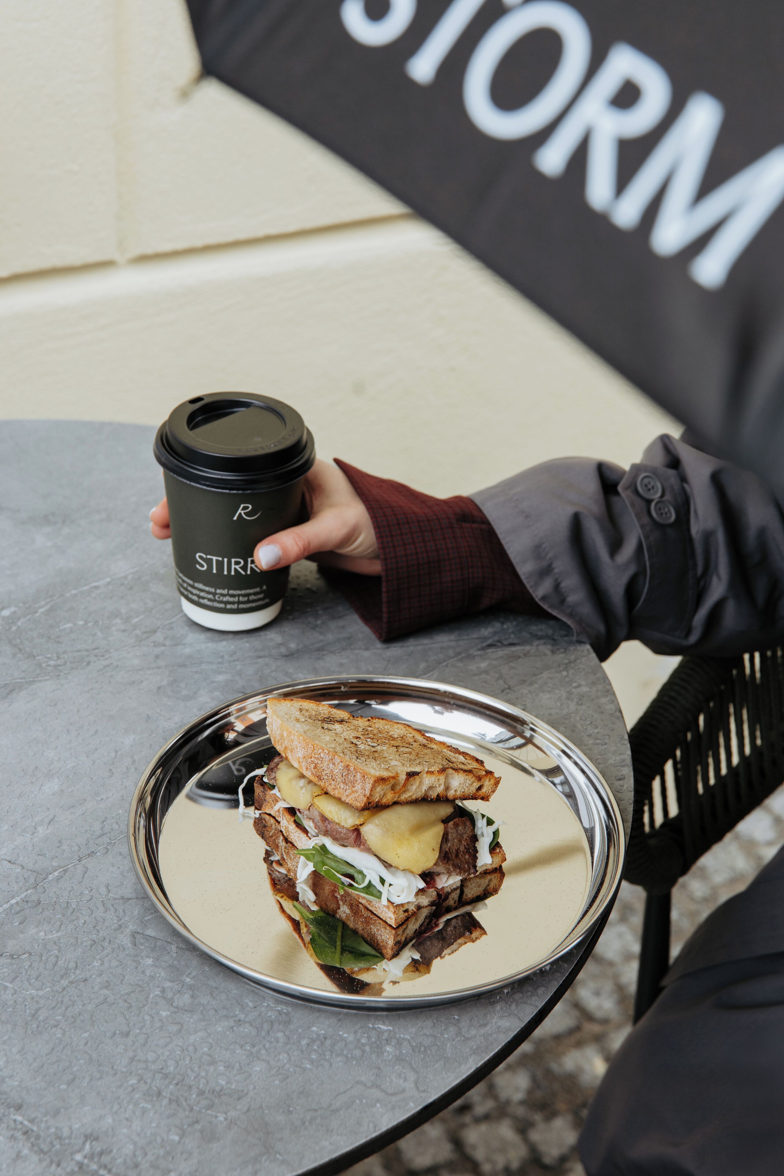Un sándwich sobre un plato de metal con una taza de café a un lado.