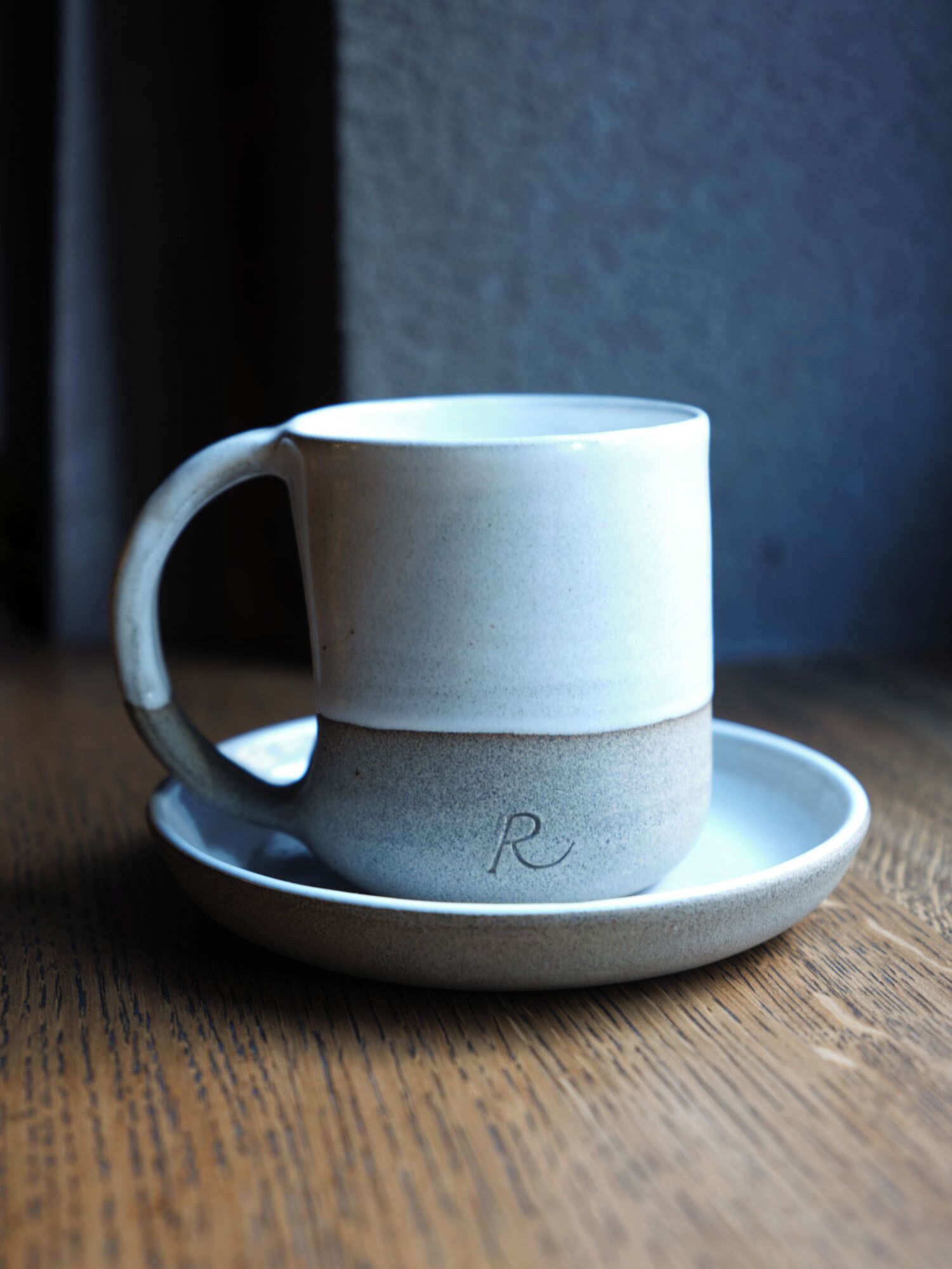 A ceramic mug with a handle and a plate, placed on a wooden surface.