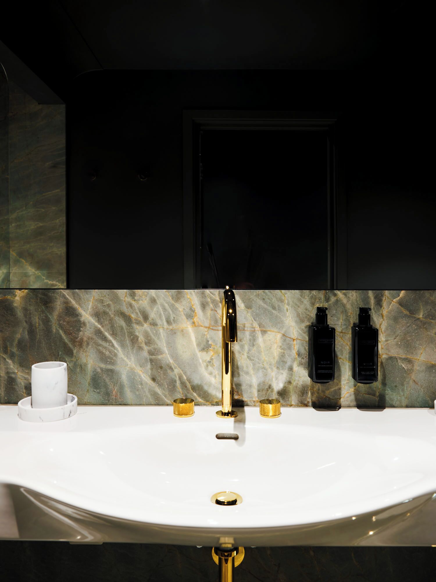 Un baño moderno con lavamanos blanco, detalles dorados y salpicadero de mármol.