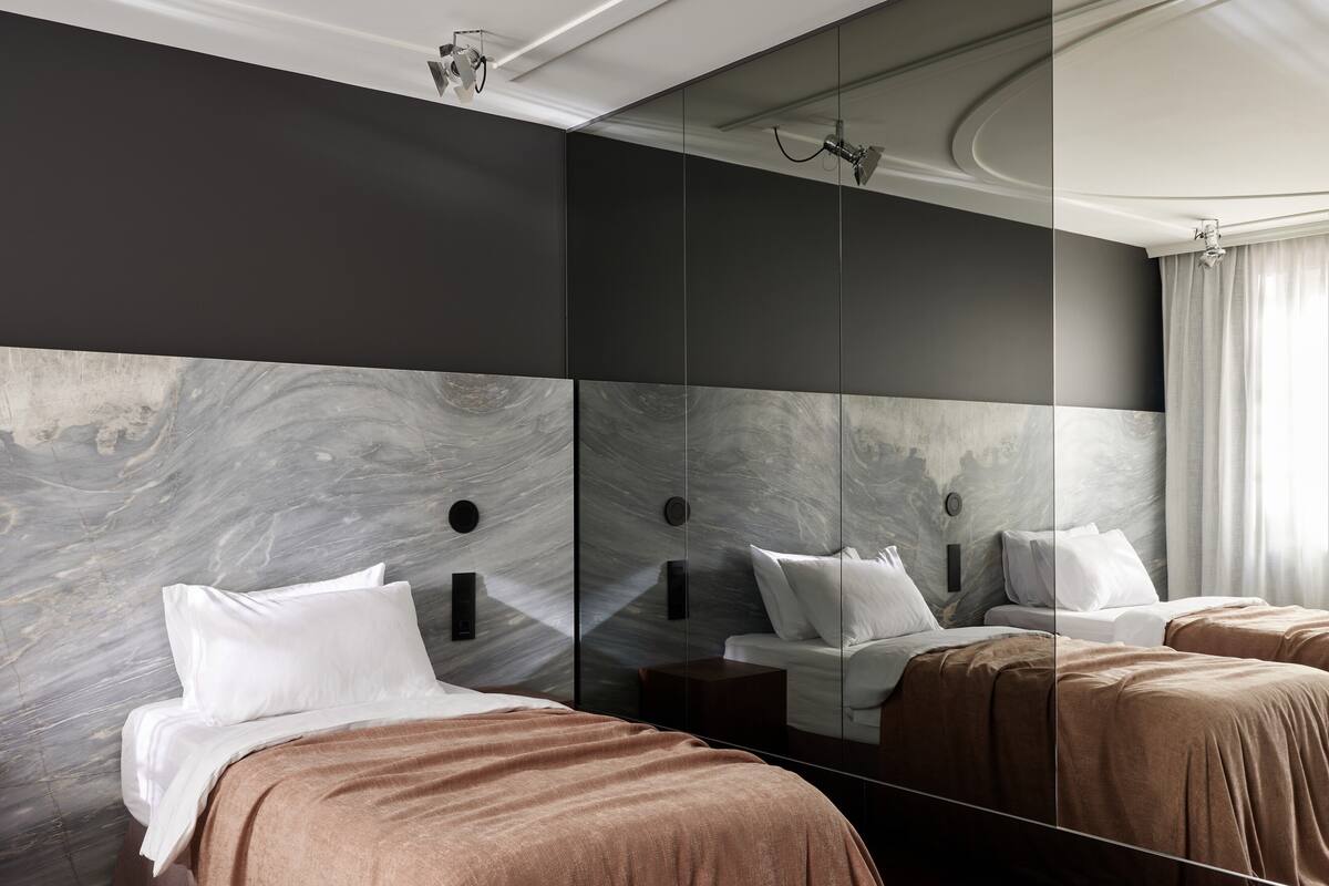 Una habitación de hotel moderna con un espejo grande, dos camas y un diseño de pared que imita el mármol.