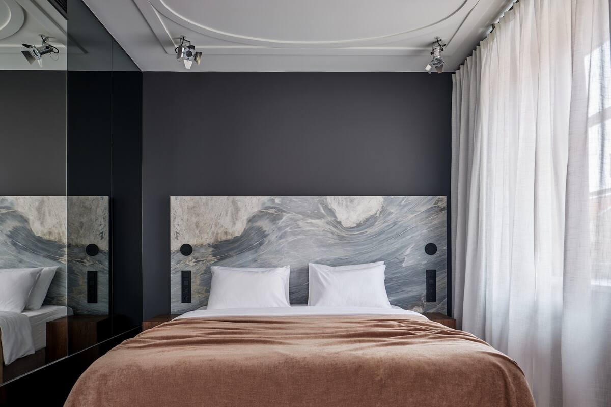 Un dormitorio moderno con una cama grande, cabecera de mármol y un espejo amplio.