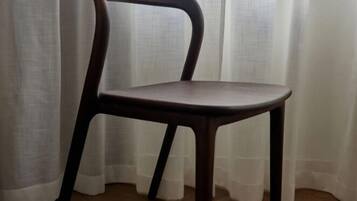 Una silla de madera con respaldo curvo y cuatro patas, ubicada frente a una ventana con cortinas traslúcidas.