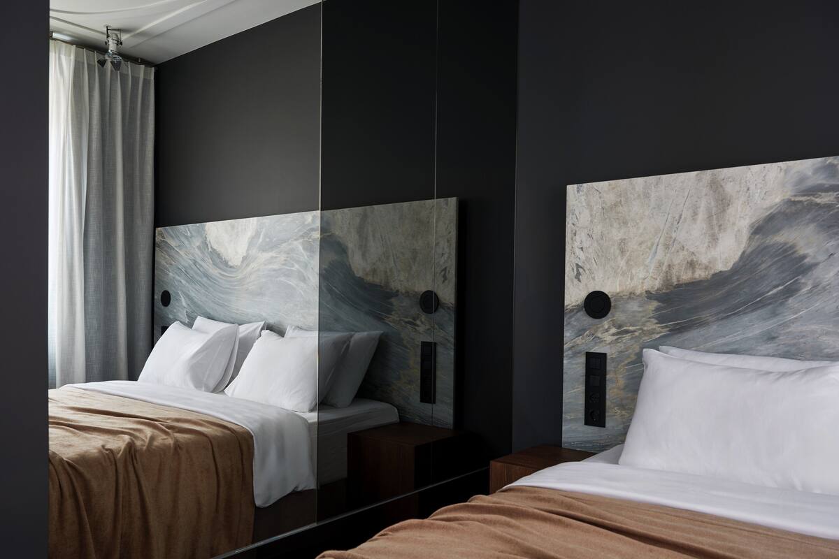 Una habitación de hotel moderna con una cama grande, una mesita de noche y un espejo que refleja el espacio.