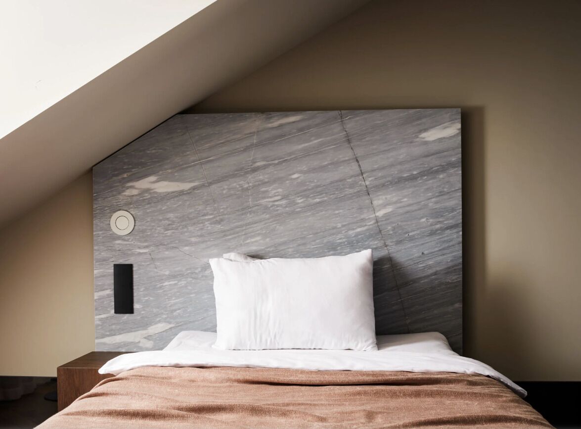 A bedroom with a sloped ceiling, a marble headboard, a white pillow, and a brown blanket.