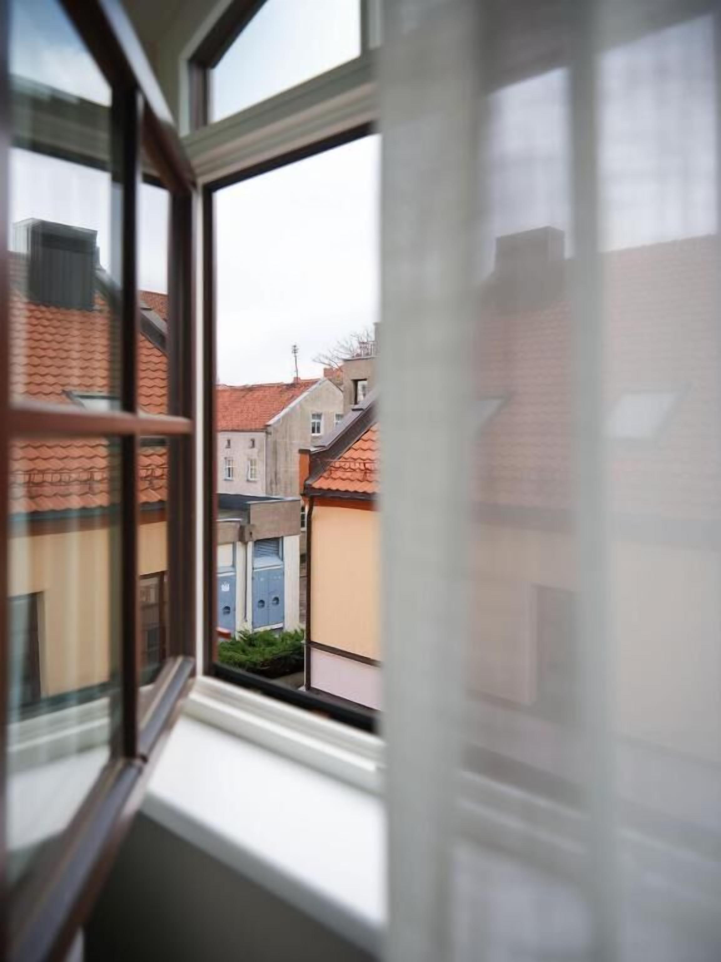 A window with a view of a residential area, including houses with red roofs and a blue door.