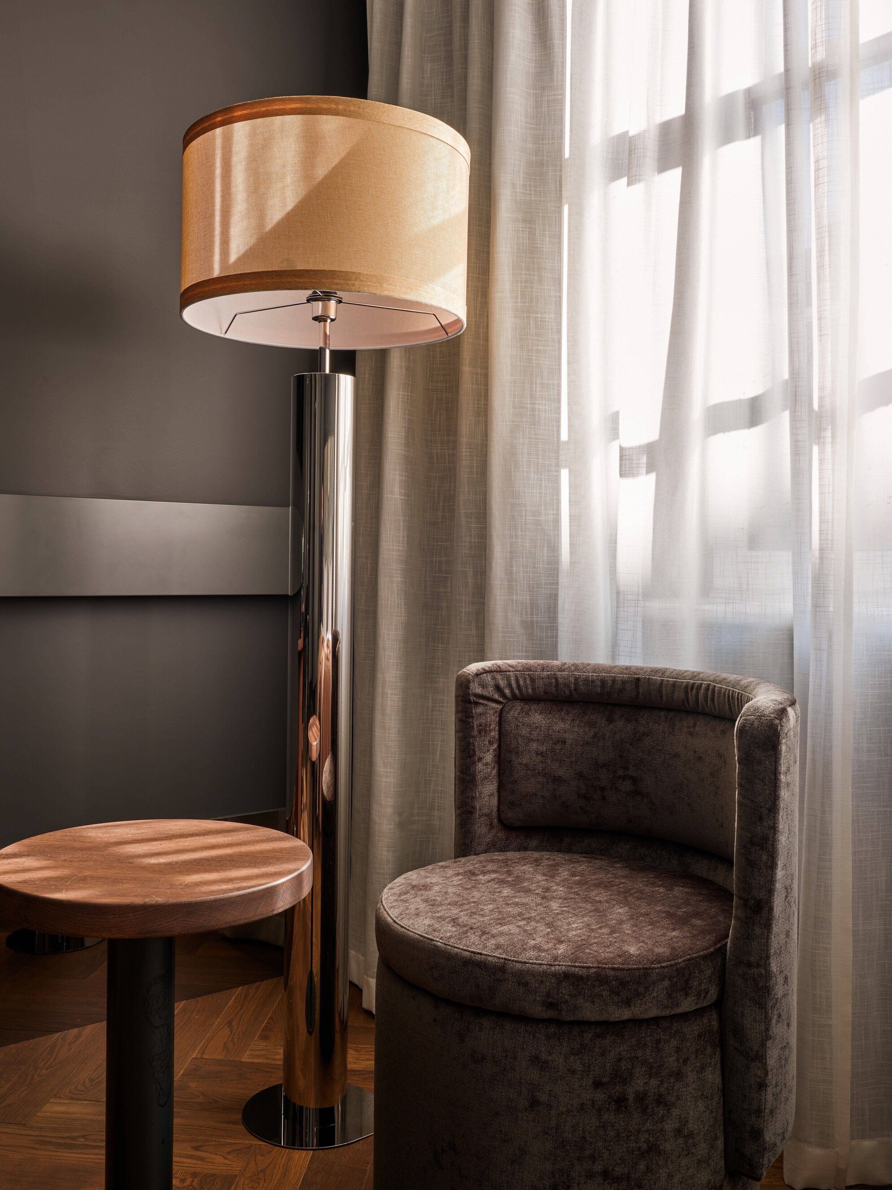 A modern room with a round wooden table, a tall floor lamp, and a plush armchair.