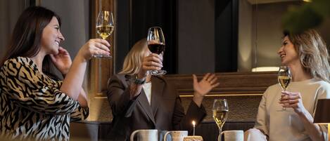 A dimly lit restaurant interior with a table set for three people, each holding a glass of wine.