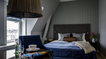 A hotel room with a bed, a table with a chair, a window, and a lamp.