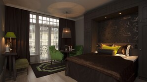 A modern hotel room with a large bed, a green chair, a small table with candles, and a view of the city through large windows. - Frogner House - Skovveien (Oslo)