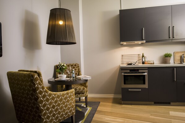 A modern kitchen with dark cabinets, a built-in oven, and a dining area with patterned chairs and a table. - Frogner House - Skovveien (Oslo)