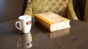 Una mesa con una taza blanca, un libro, una lámpara y una silla estampada.