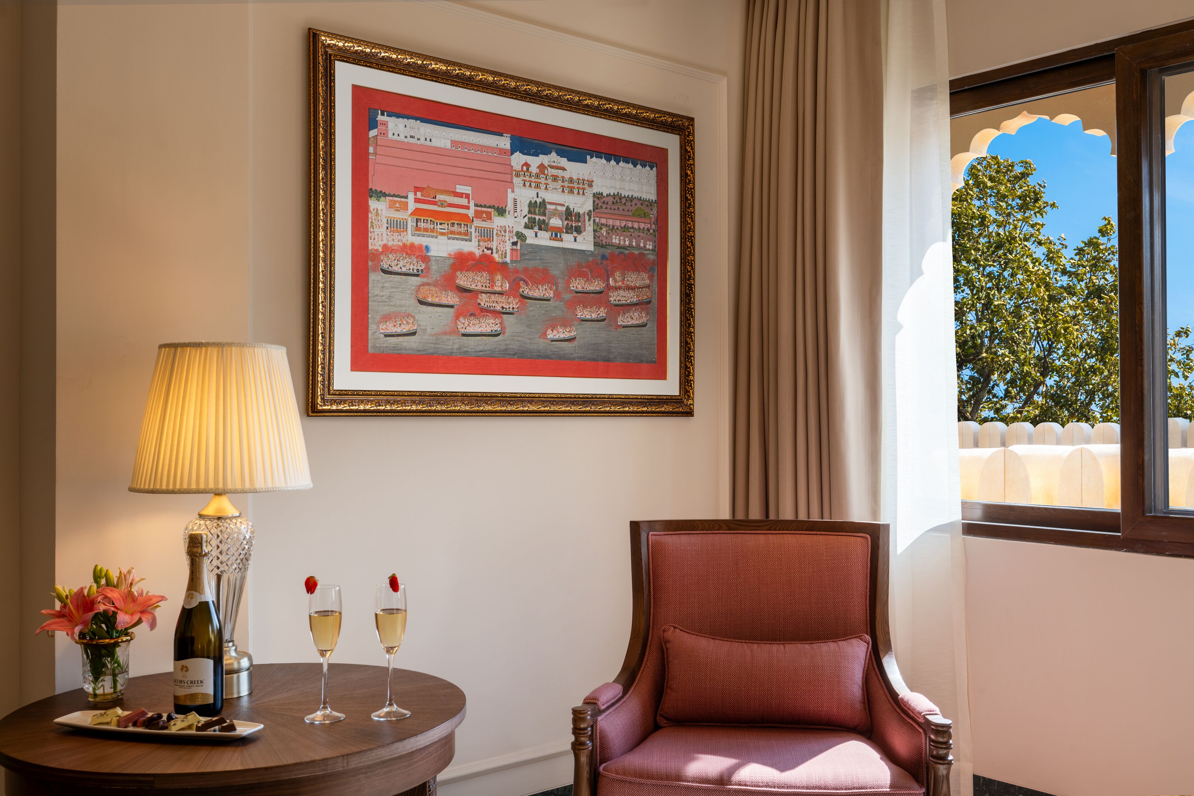 Une pièce avec un tableau encadré, une table avec une lampe, deux verres de vin et une chaise.