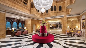 A lobby with a central red circular seating area, a reception desk with staff, and a chandelier. - Taj Gorbandh Palace, Jaisalmer (Jaisalmer)