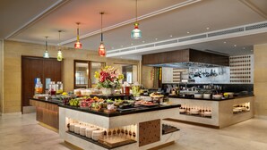A spacious hotel kitchen with a buffet area, featuring a marble countertop, hanging lights, and a variety of food and drink options. - Taj Gorbandh Palace, Jaisalmer (Jaisalmer)