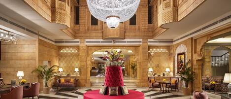 A grand lobby with a large chandelier, a central red seating area, and a checkered marble floor.