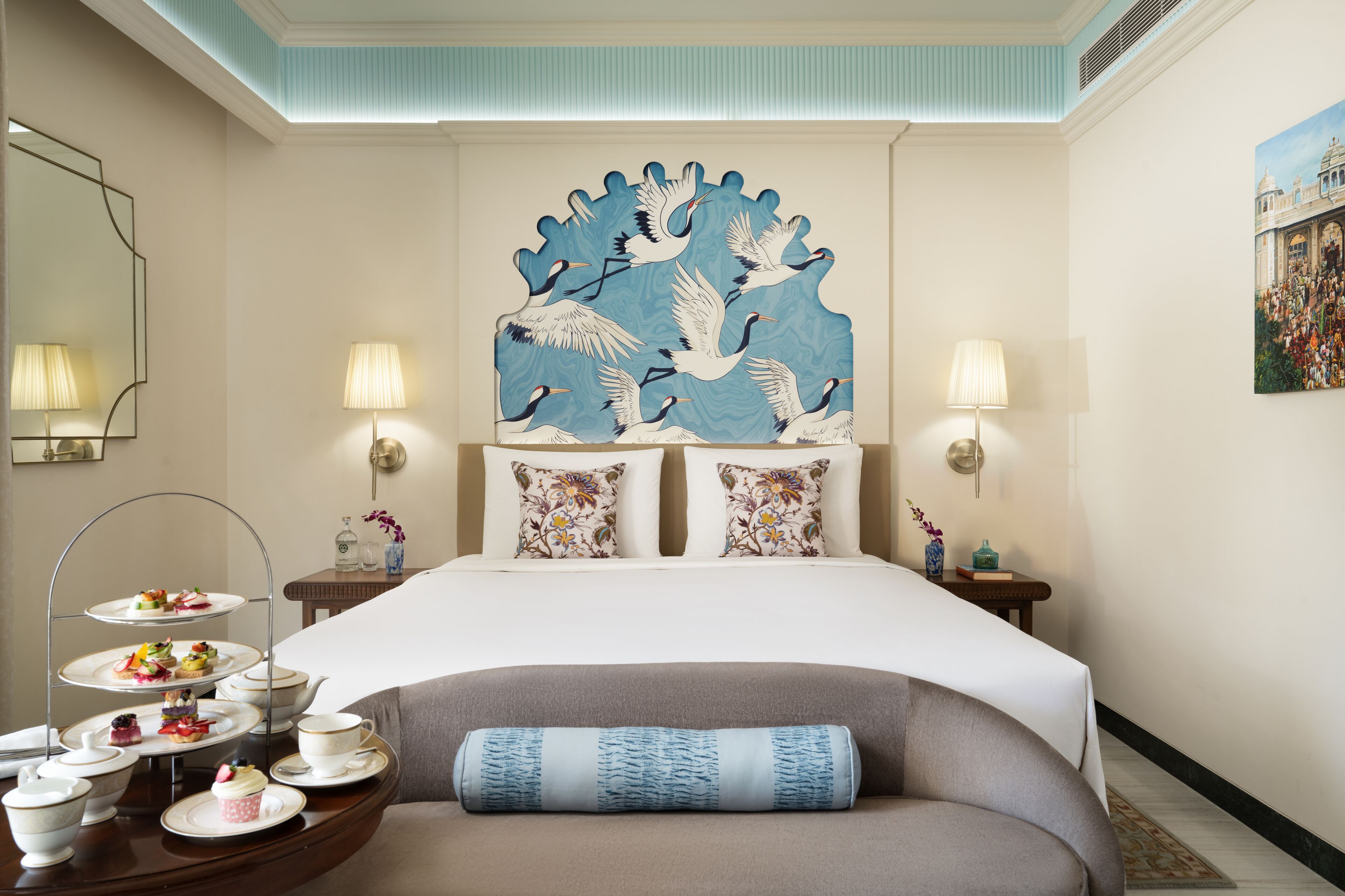 Hotelkamer met een groot bed, twee nachtkastjes, een decoratief wandobject en een dienblad met thee en gebak.